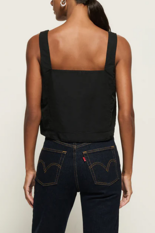 Person wearing a black sleeveless top and dark blue jeans with a Levi's logo on a light background
