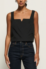 Person wearing a black sleeveless top and dark jeans on a plain background