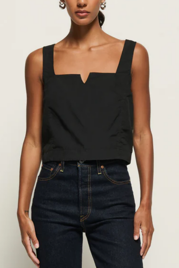Person wearing a black sleeveless top and dark jeans on a plain background