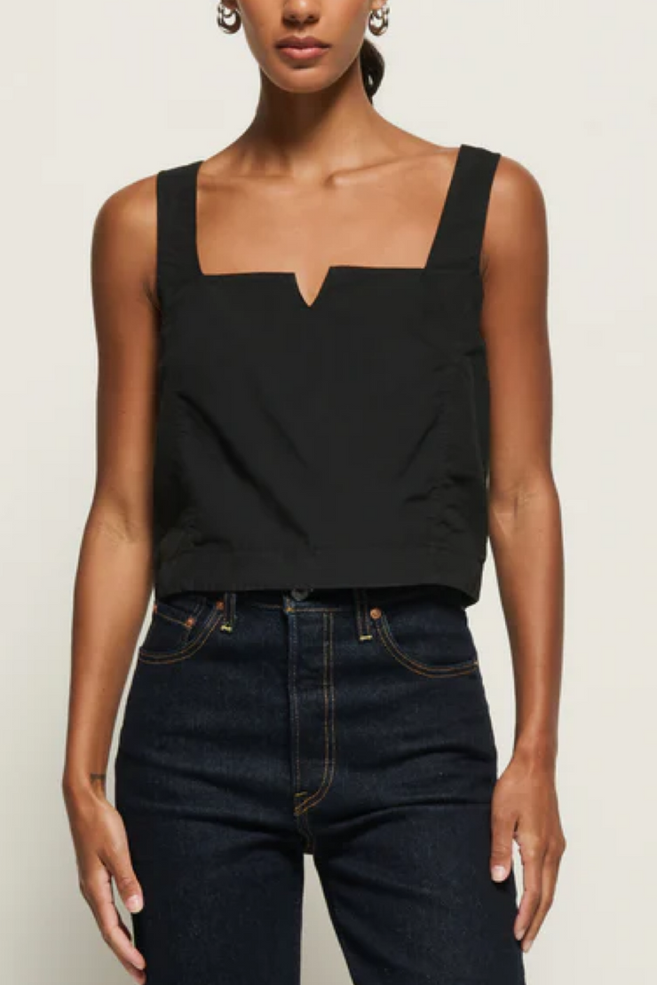 Person wearing a black sleeveless top and dark jeans on a plain background