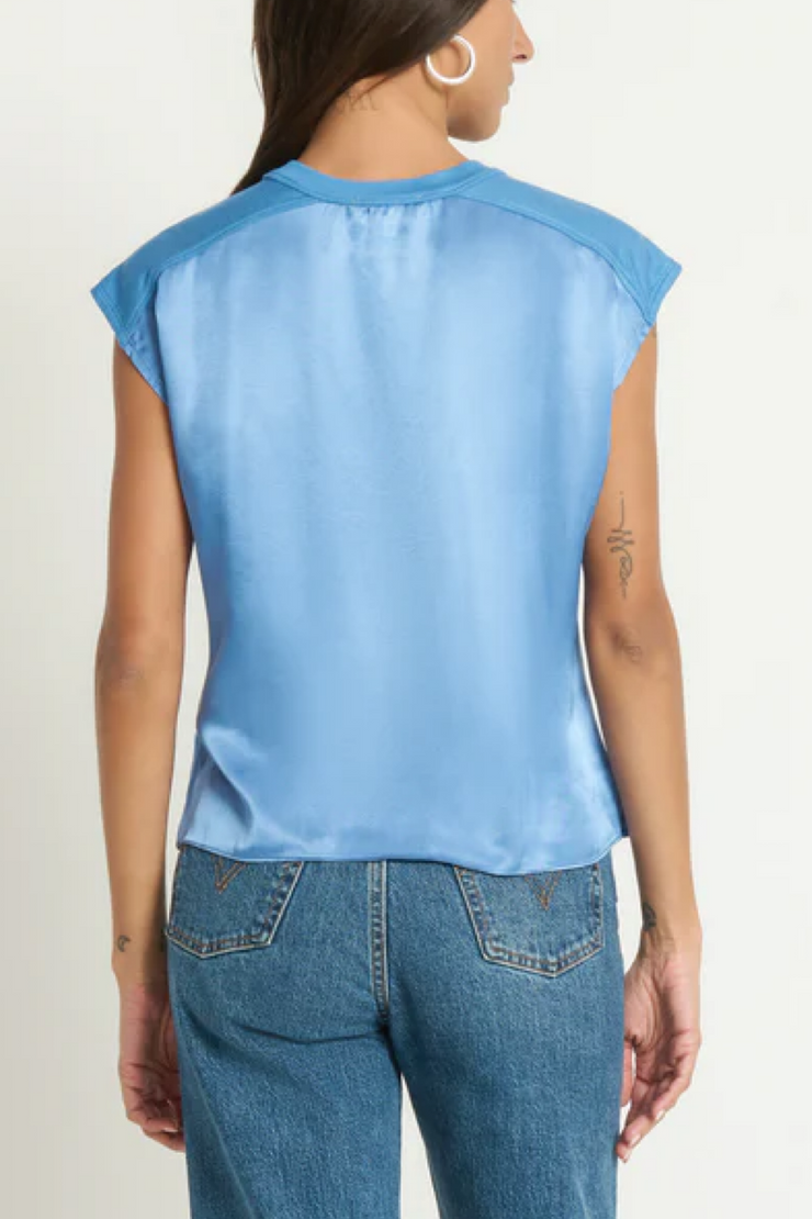 Person wearing a light blue sleeveless top and blue jeans on a plain background