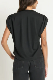 Person wearing a black sleeveless top and dark jeans on a plain background
