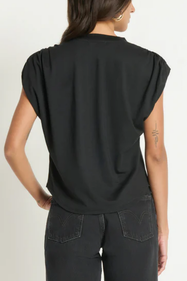 Person wearing a black sleeveless top and dark jeans on a plain background