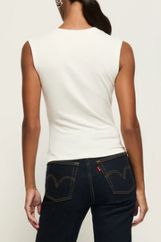 Person wearing a sleeveless top and dark blue jeans with Levi's logo on a plain background