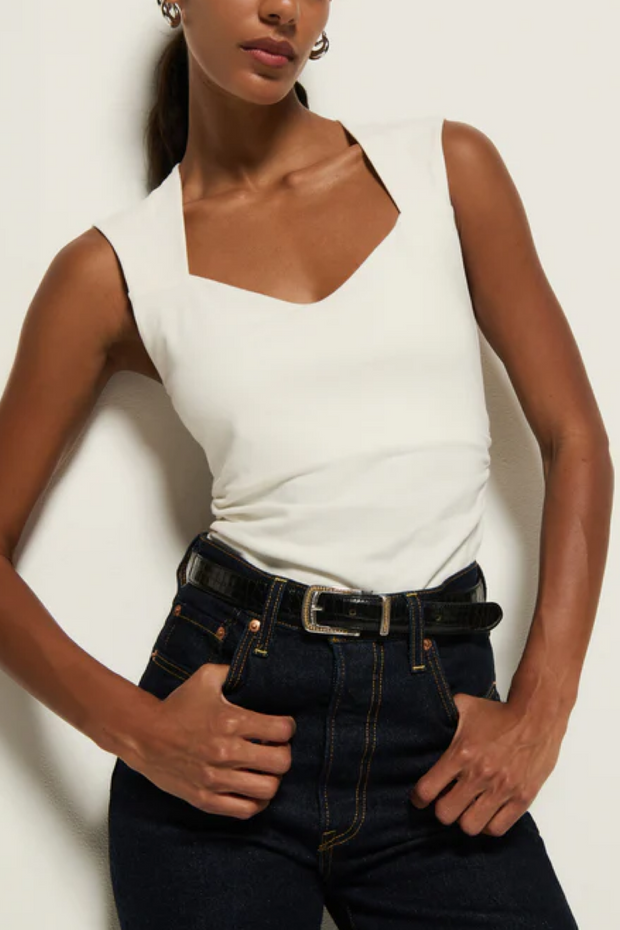 Person wearing a  sleeveless top and dark jeans against a plain background
