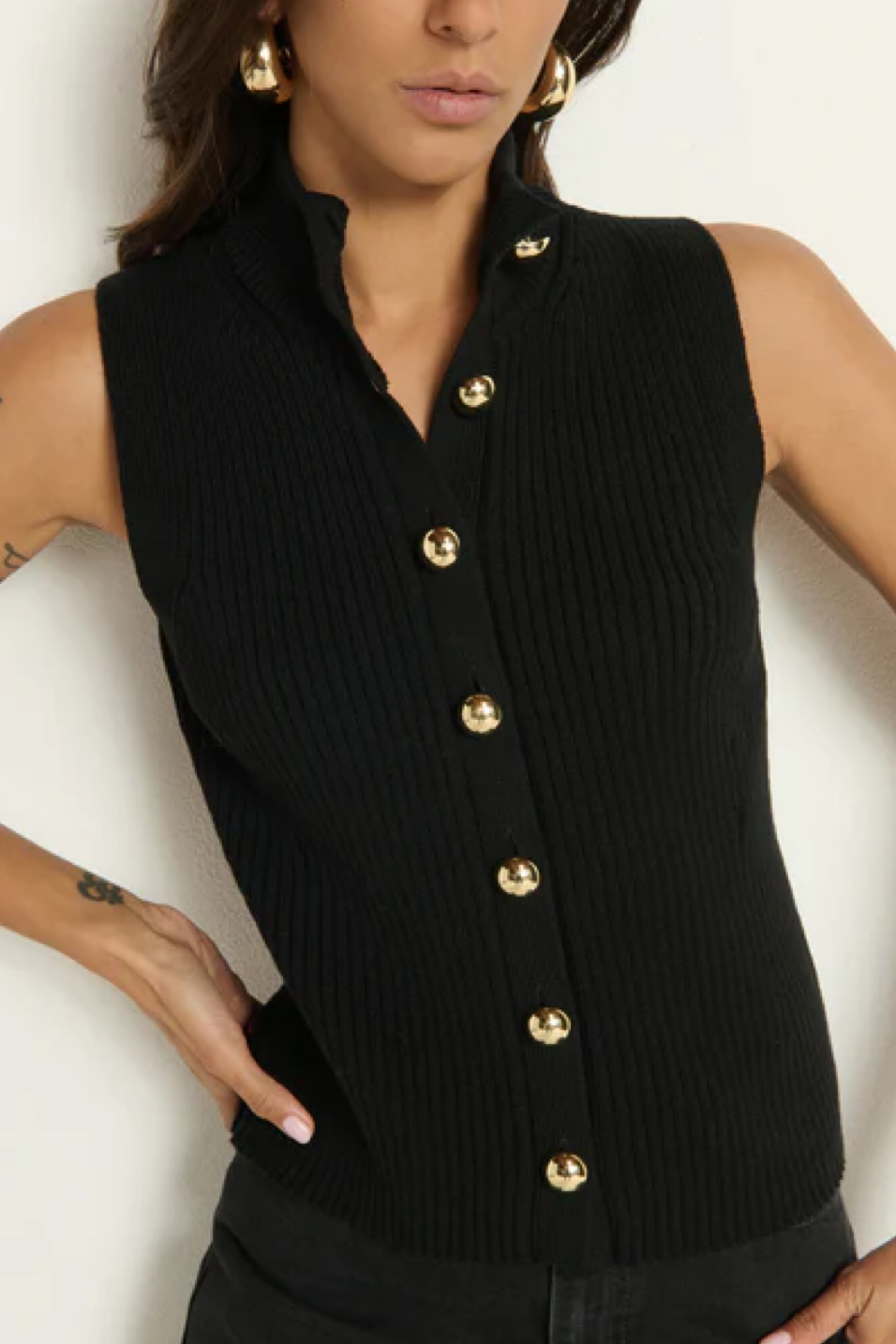 Black sleeveless button-up top with gold buttons worn by a model on a white background
