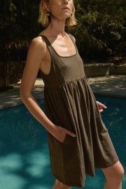 Woman wearing a brown dress by a poolside with trees in the background