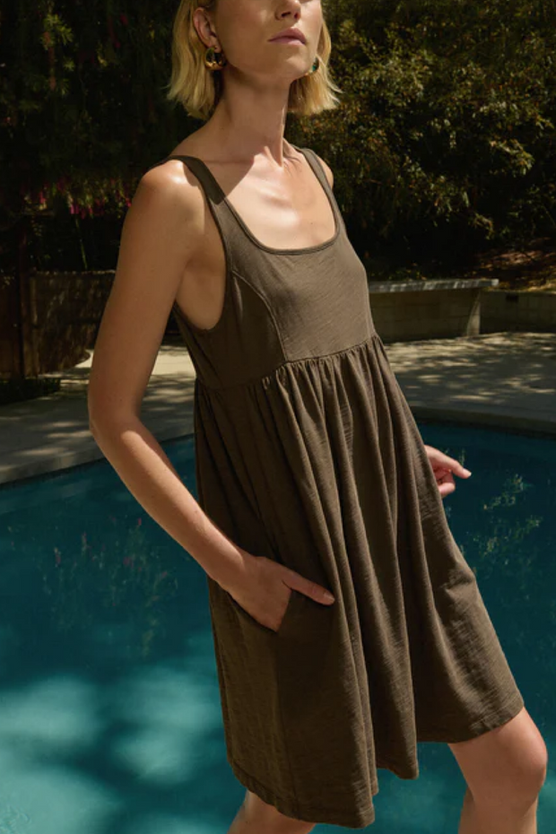 Woman wearing a brown dress by a poolside with trees in the background