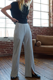 Person wearing a black tee and light gray wide-leg sweatpants in a room with brick walls and a brown couch.