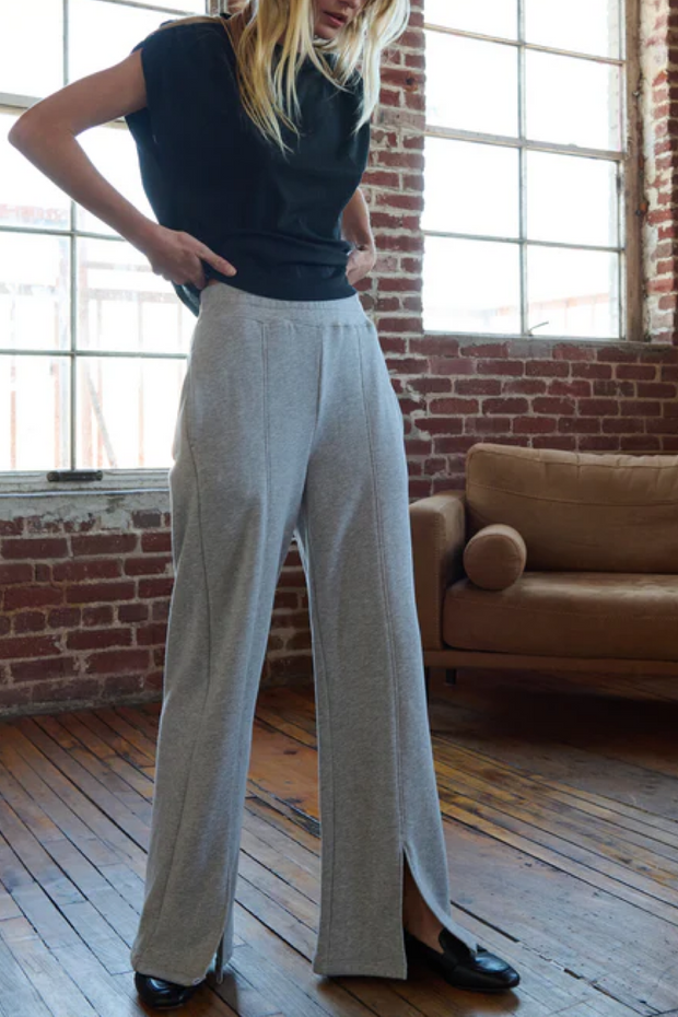 Person wearing a black tee and light gray wide-leg sweatpants in a room with brick walls and a brown couch.