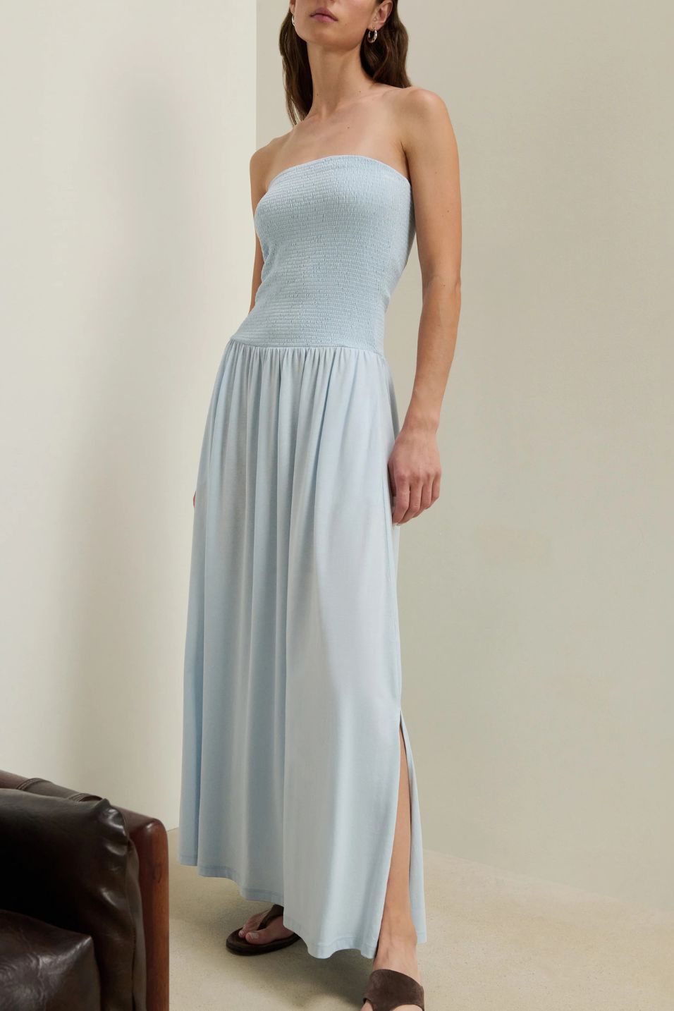 Woman wearing a light blue strapless dress with a slit on a plain background