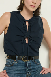 Person wearing a navy sleeveless top with a cutout design and high-waisted jeans on a white background