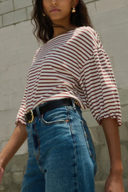 Person wearing a striped shirt and blue jeans against a gray wall.
