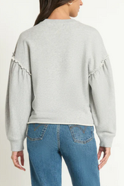 Person wearing a light gray sweatshirt with ruffled sleeves and blue jeans on a white background