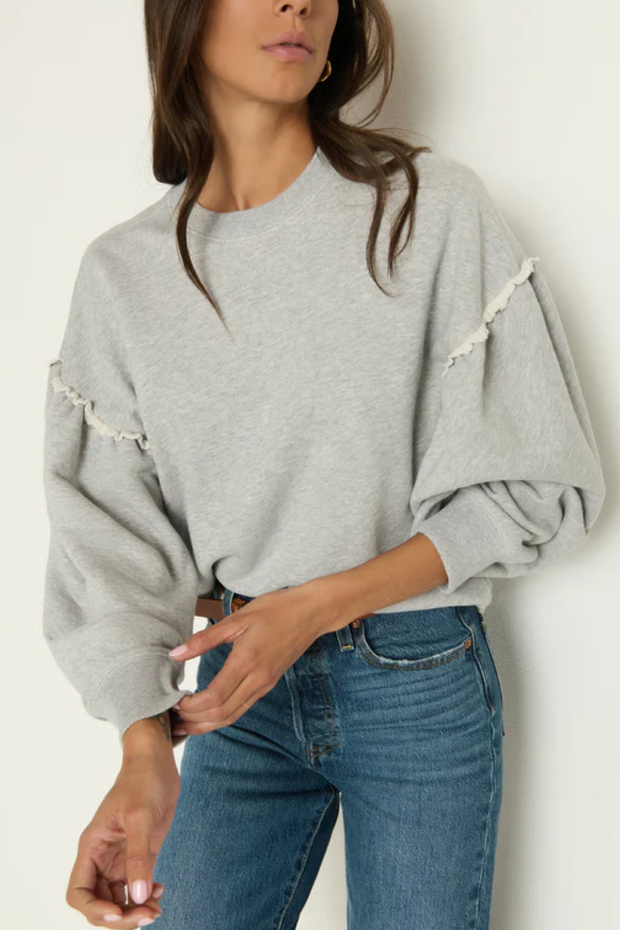 Woman wearing a grey sweatshirt with details and blue jeans against a white background