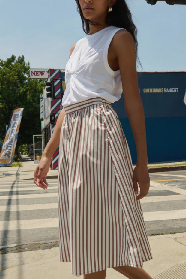 Woman wearing a white top and striped skirt on a city street.