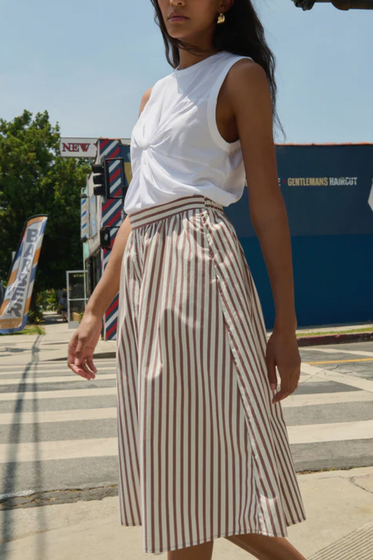 Woman wearing a white top and striped skirt on a city street.