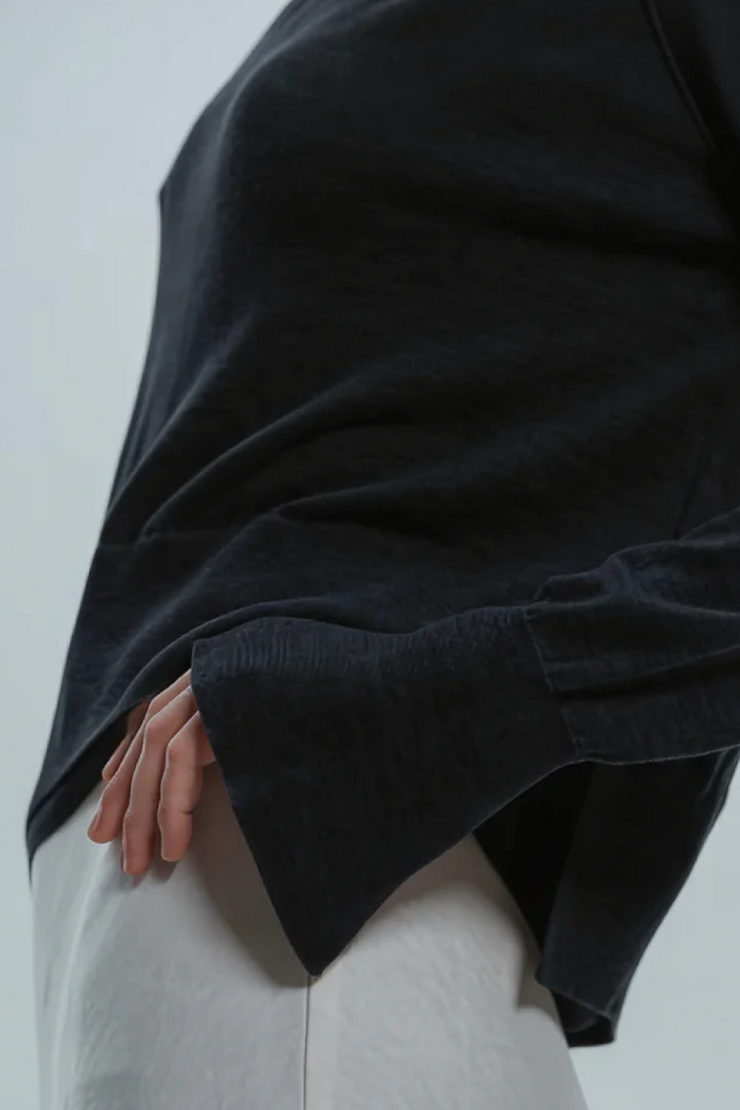 Person wearing a black sweater over a light-colored outfit on a plain background