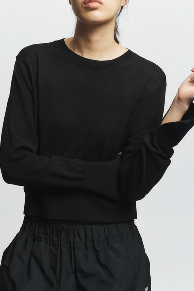 Person wearing a black long-sleeve top and black pants on a light gray background