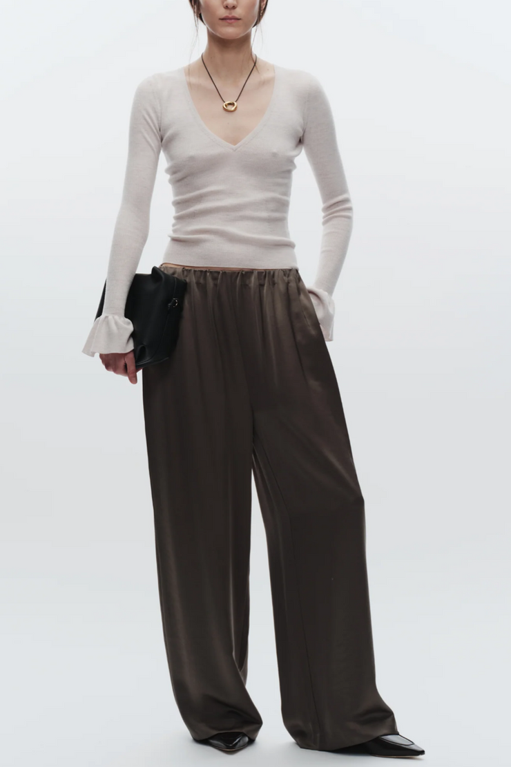 Person wearing a white long-sleeve top and dark wide-leg pants on a white background