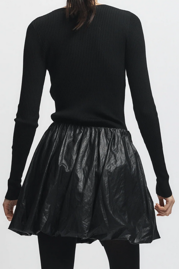 Person wearing a black ribbed sweater and black leather skirt on a white background