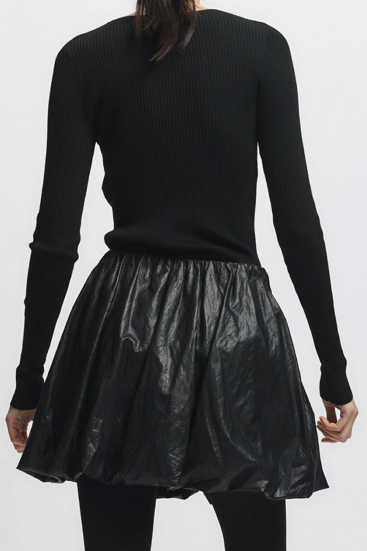 Person wearing a black ribbed sweater and black leather skirt on a white background