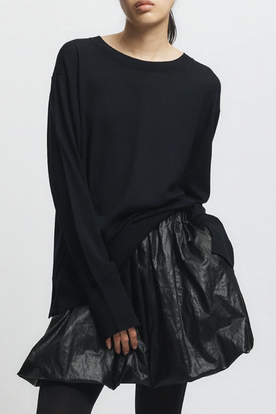 Person wearing a black oversized top with a shiny black skirt on a white background