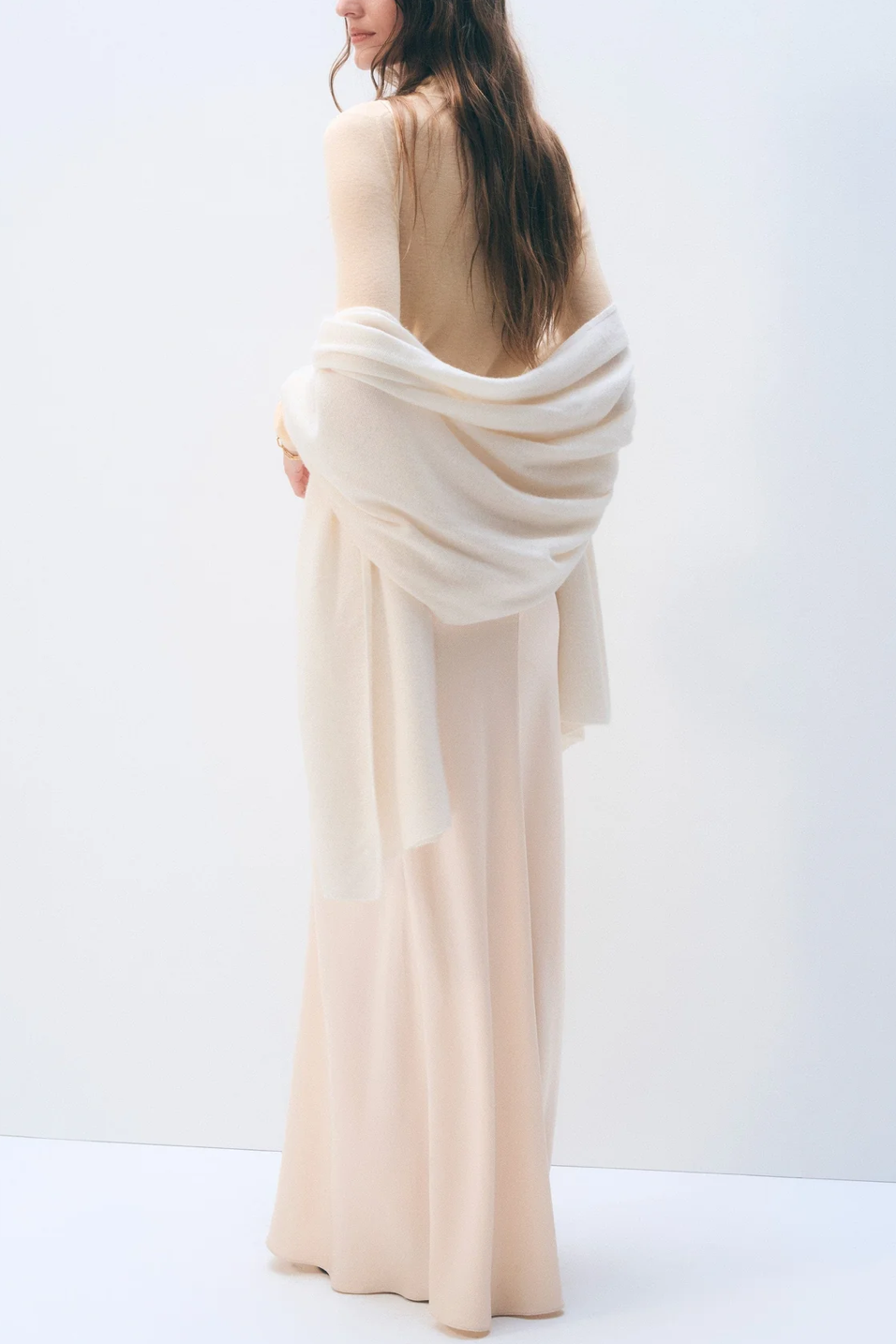Woman wearing a long, flowing beige dress with a white scarf against a white background