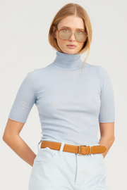 Person wearing a light blue ribbed turtleneck top and light blue pants with a tan belt.