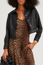 Person wearing a black leather jacket over a leopard print dress on a white background