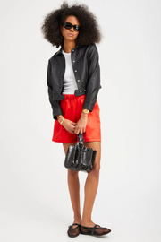 Woman wearing a black leather jacket, white shirt, red shorts, and black shoes on a white background