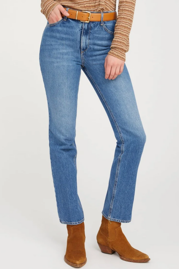 Person wearing blue jeans and brown boots on a white background