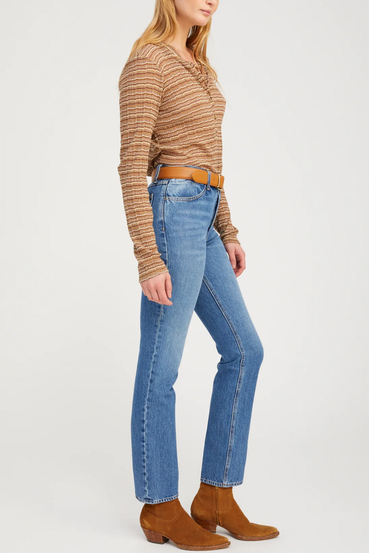 Woman wearing a brown striped sweater, blue jeans, and brown boots on a white background