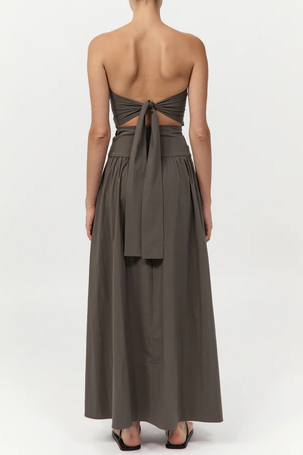 Woman wearing a strapless, long khaki dress with cut-out back on a white background