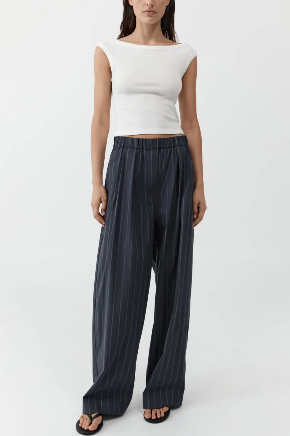 Woman wearing a white sleeveless top and dark pinstripe pants on a white background