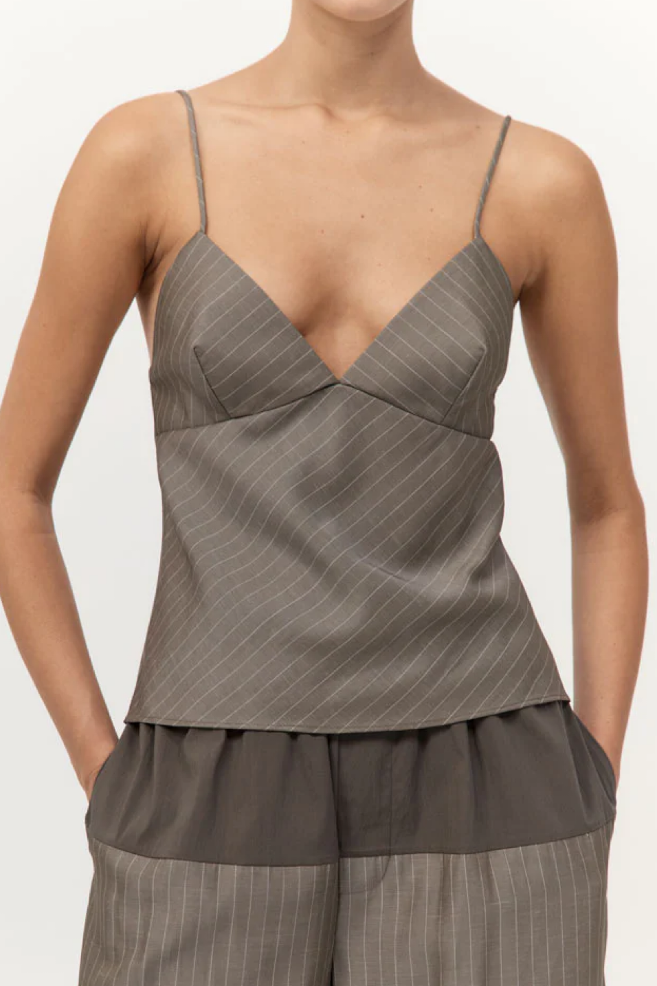 Woman wearing a khaki pinstripe top and pants on a white background