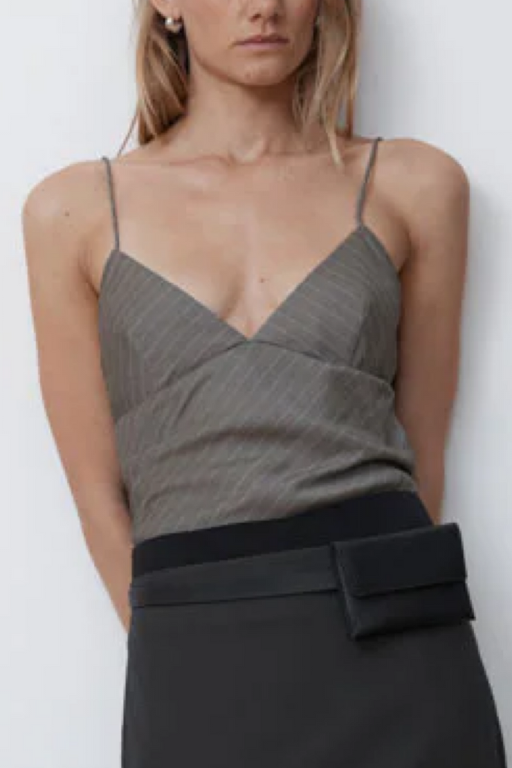 Woman wearing a khaki pinstripe top and black skirt against a white background