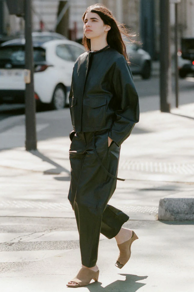 Woman in a black leather outfit walking on a city street.