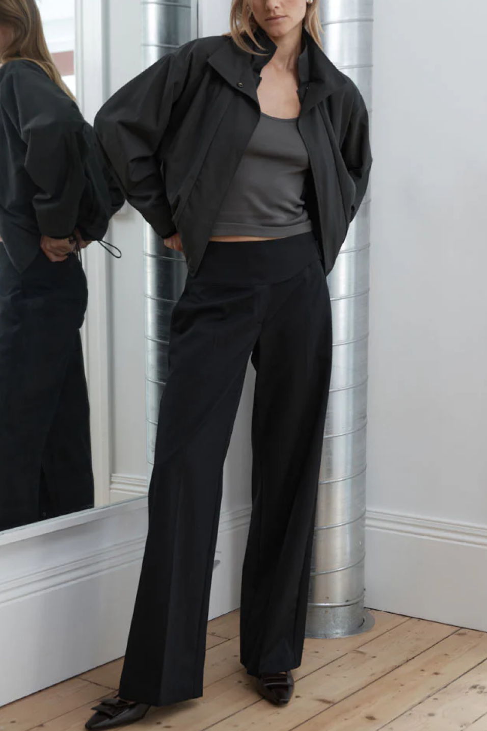 Person wearing a black outfit standing in front of a mirror.