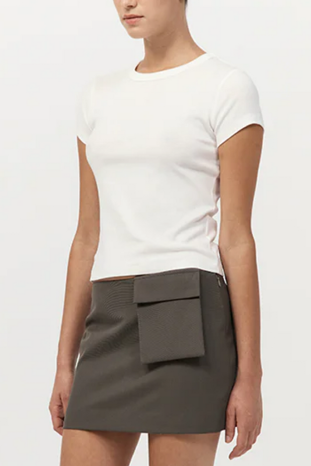 Person wearing a white t-shirt and gray skirt with a pocket on a plain background