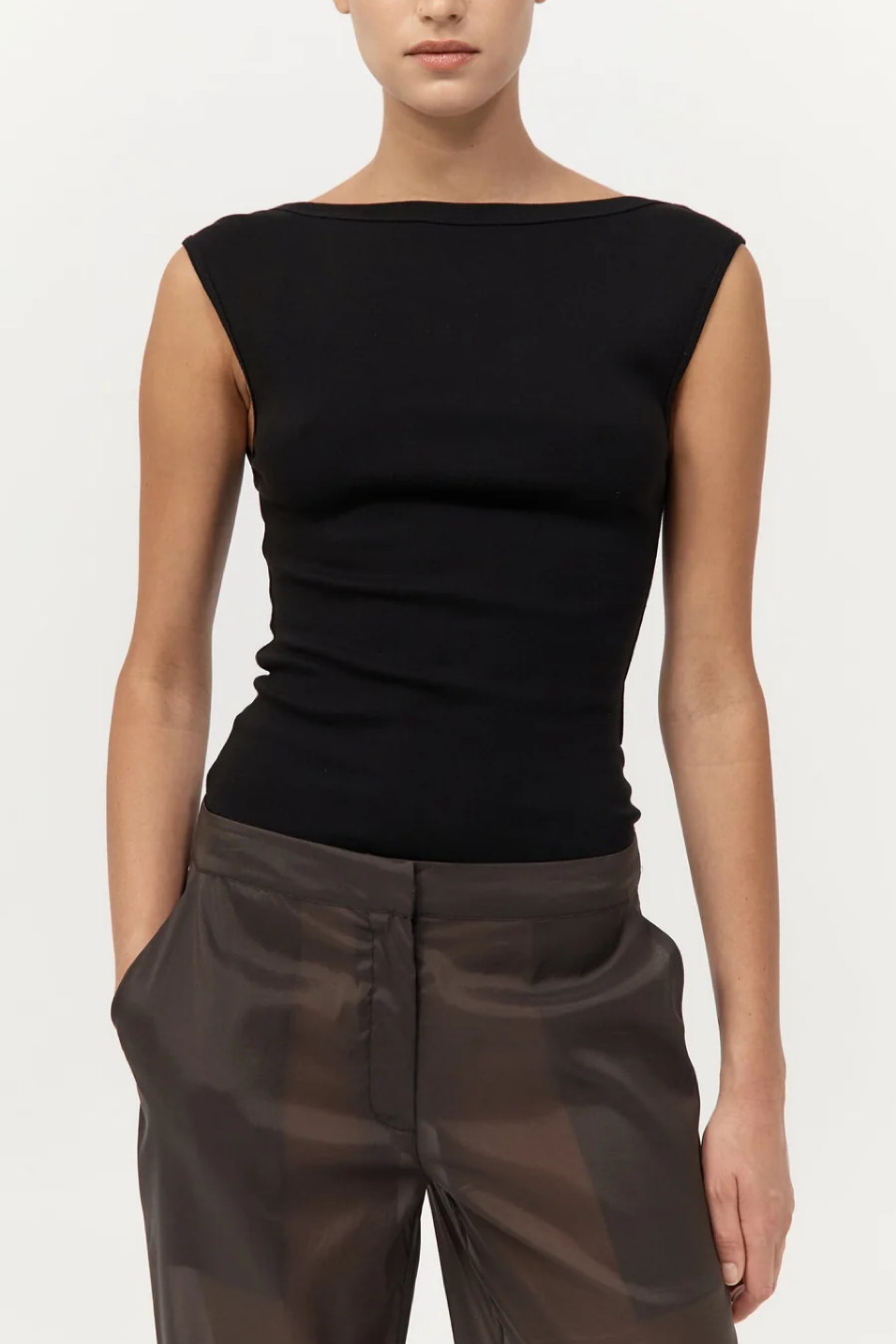 Person wearing a black sleeveless top and brown pants on a white background