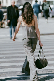 Woman wearing khaki pinstripe top and pants walking on a city street with a black handbag.