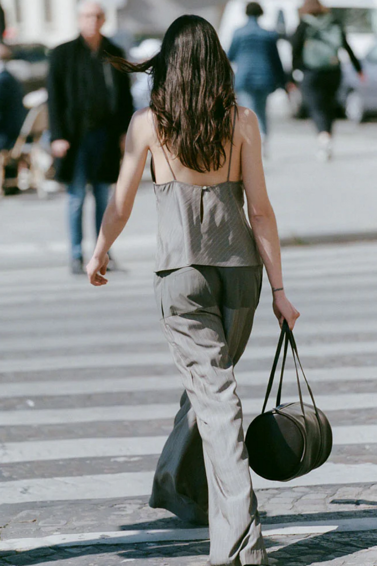 Woman wearing khaki pinstripe top and pants walking on a city street with a black handbag.