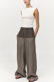 Person wearing a white sleeveless top and khaki pinstripe wide-leg pants on a white background