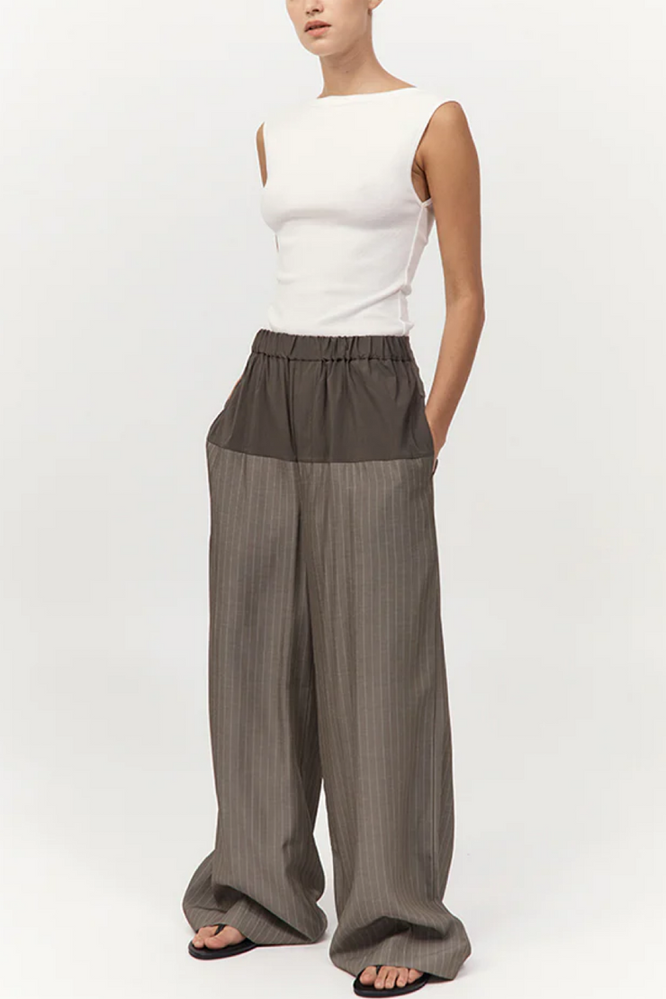 Person wearing a white sleeveless top and khaki pinstripe wide-leg pants on a white background
