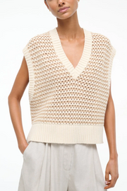 Woman wearing a beige knitted sleeveless top against a white background