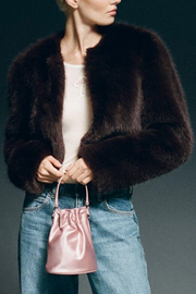 Person wearing a brown fur coat holding a pink drawstring bag against a dark background
