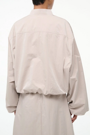 Person wearing a beige long-sleeve jacket and skirt on a white background