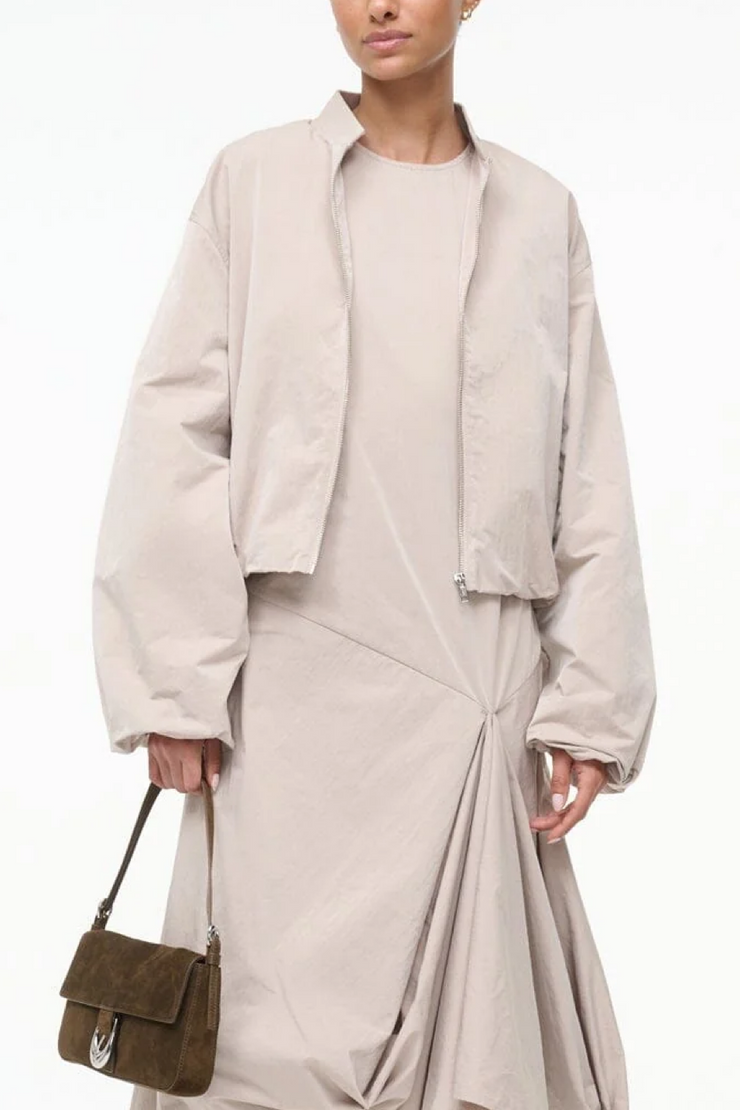 Person wearing a beige jacket and dress holding a brown bag on a white background