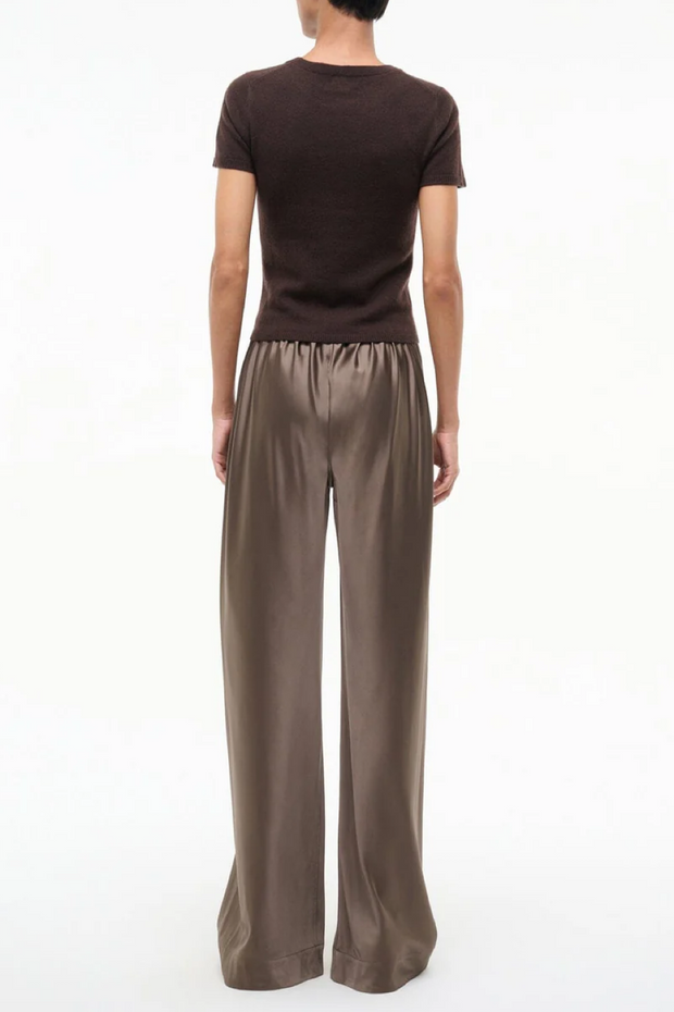 Person wearing a brown t-shirt and wide-leg silk truffle colored pants on a white background